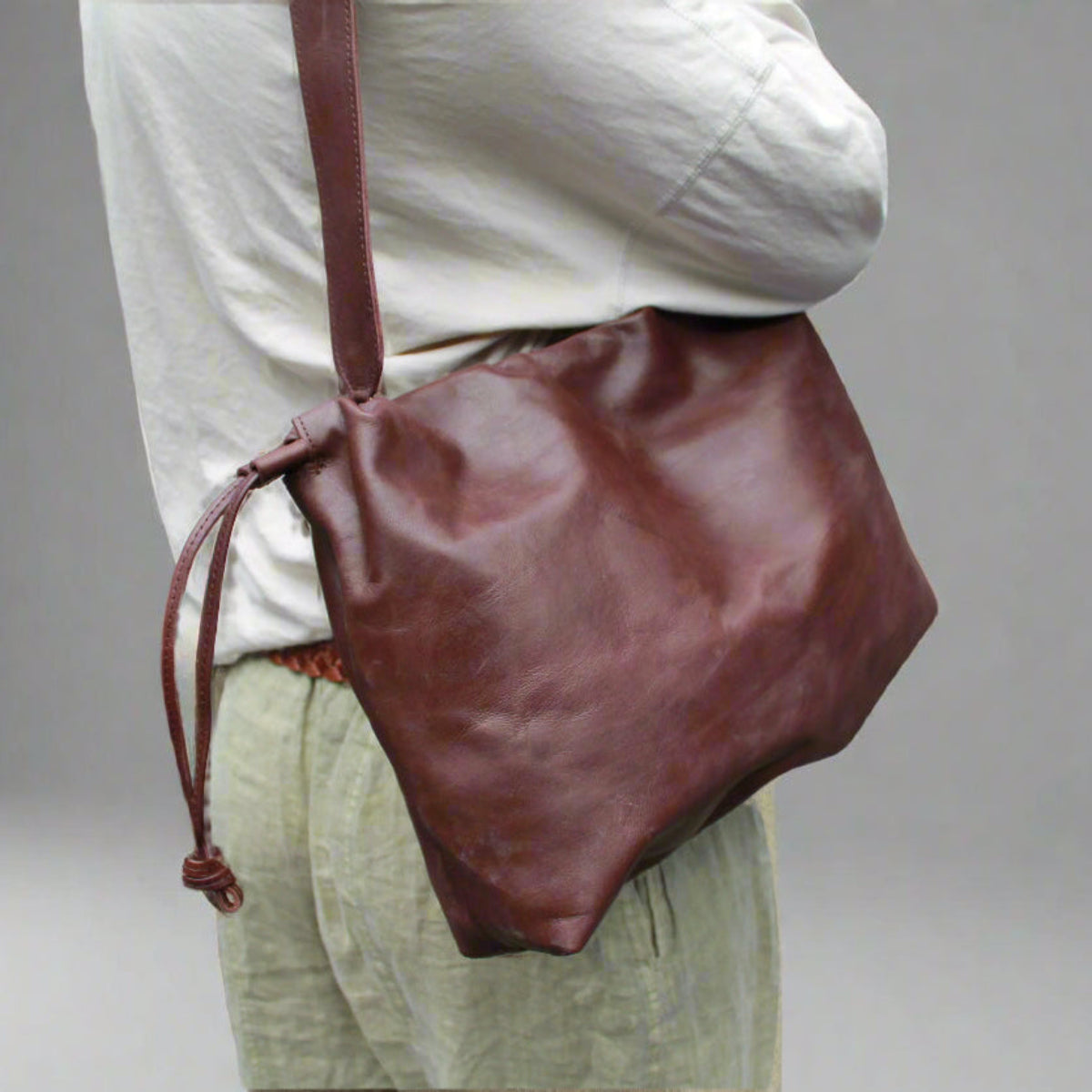 Brown leather bag worn over shoulder on a plain background